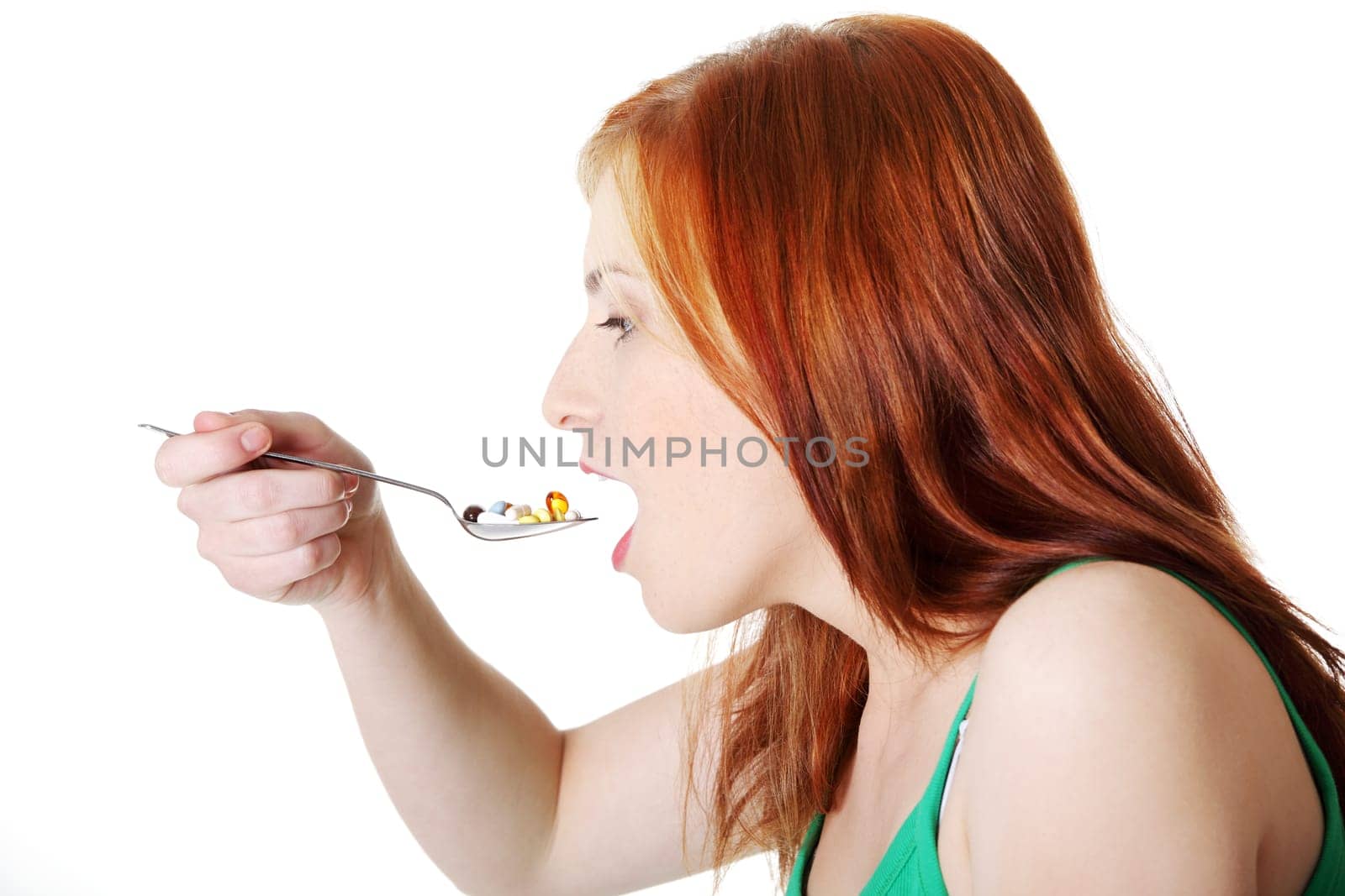 Teen beautiful caucasian girl taking pills from spoon over white background.