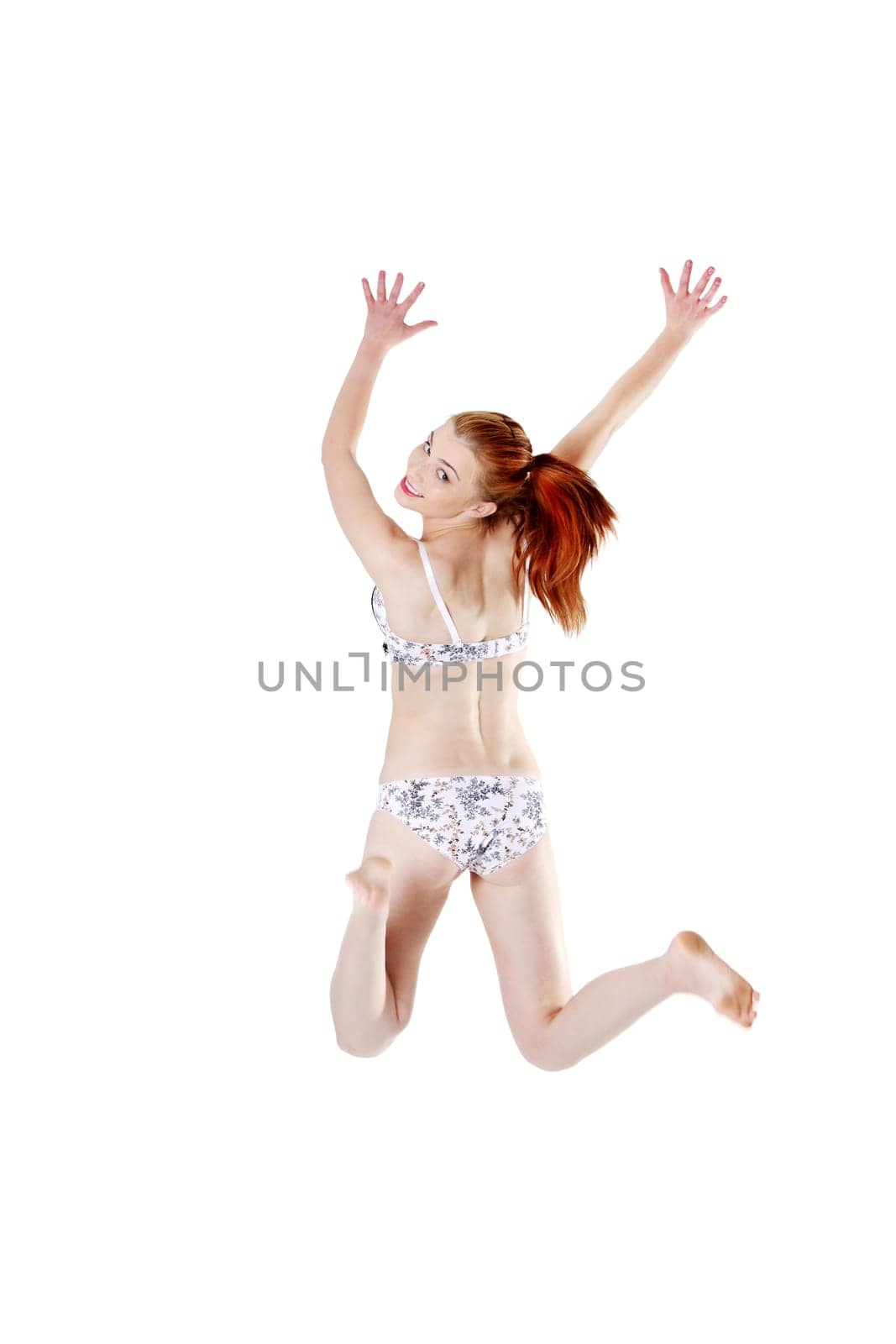 Back view of a smiling young girl jumping and having her hands up, isolated on white background.