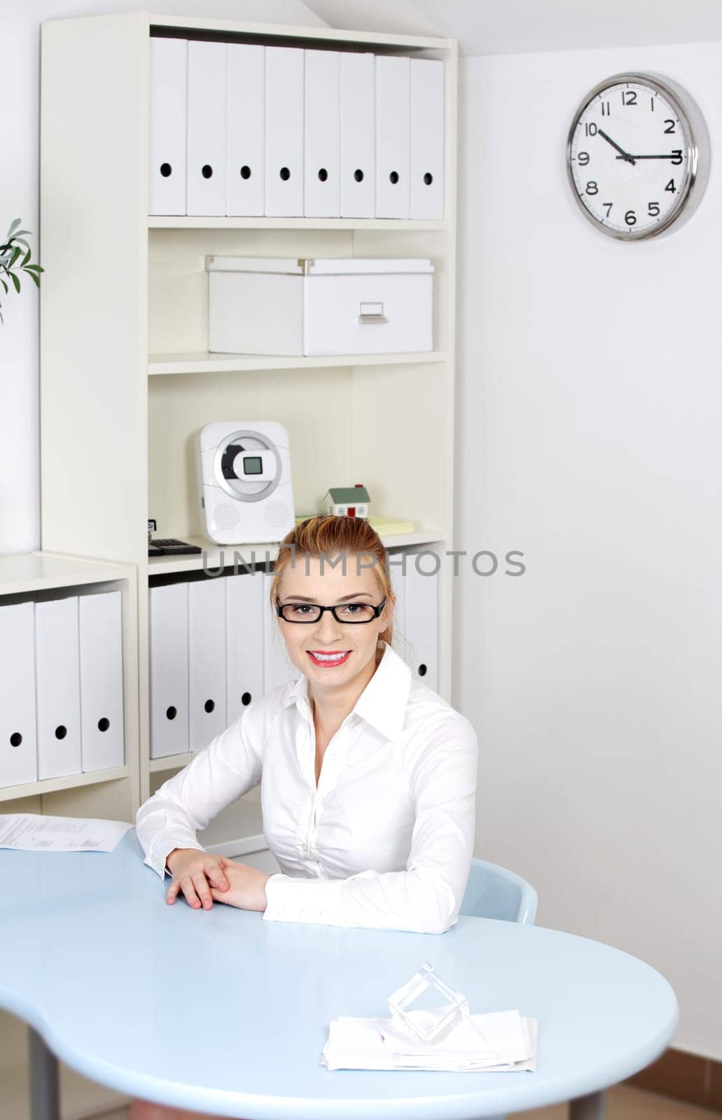 Pretty smiling girl in glasses sitting behind the desk in her office.