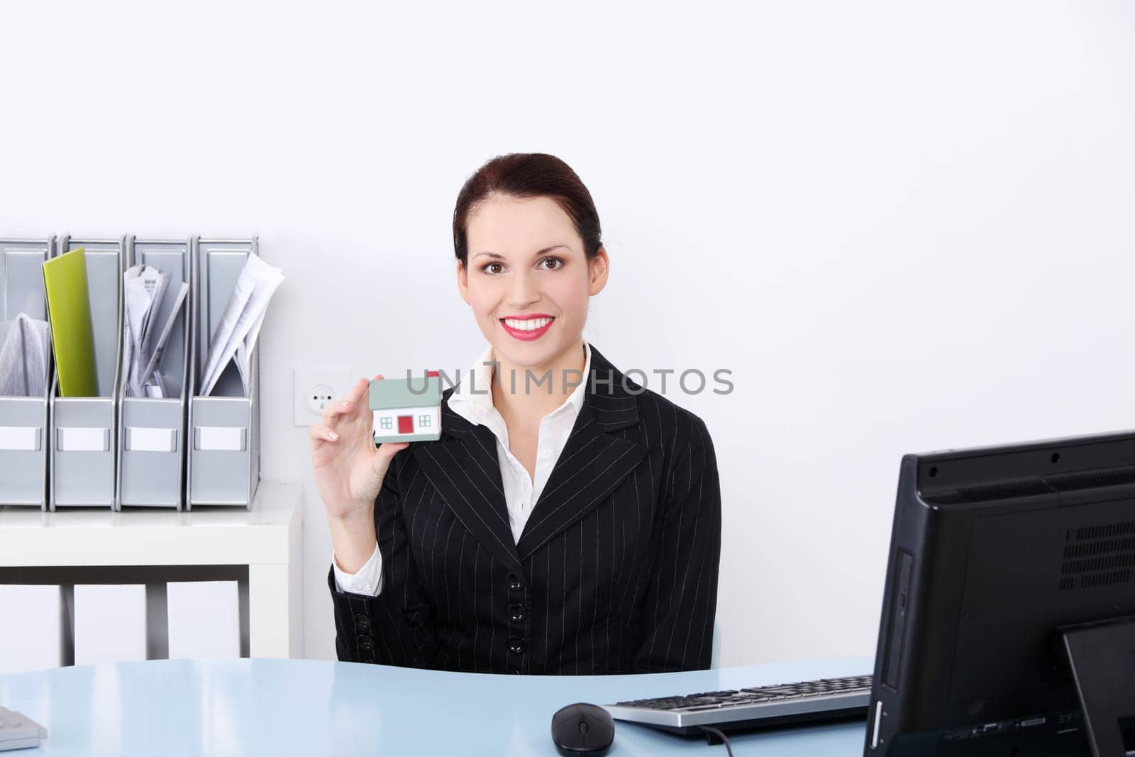 Beautiful caucasian businesswoman sitting in the office holding little house.