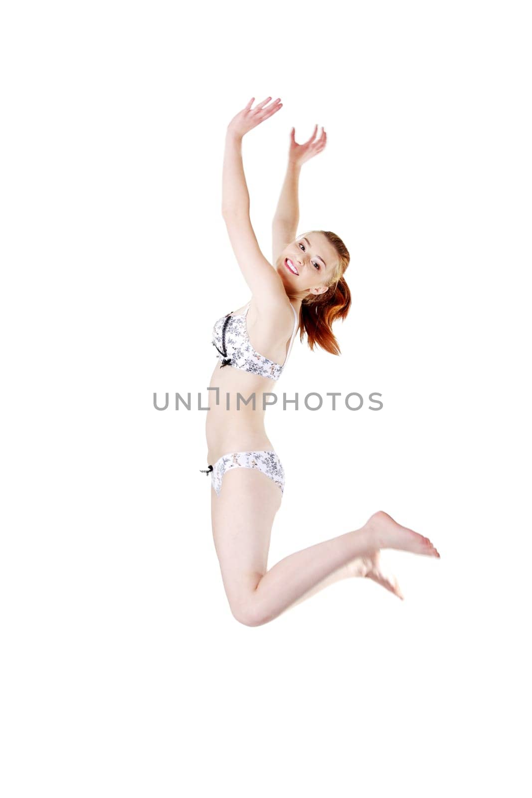 Site view of a smiling young girl jumping and having her hands up, isolated on white background.