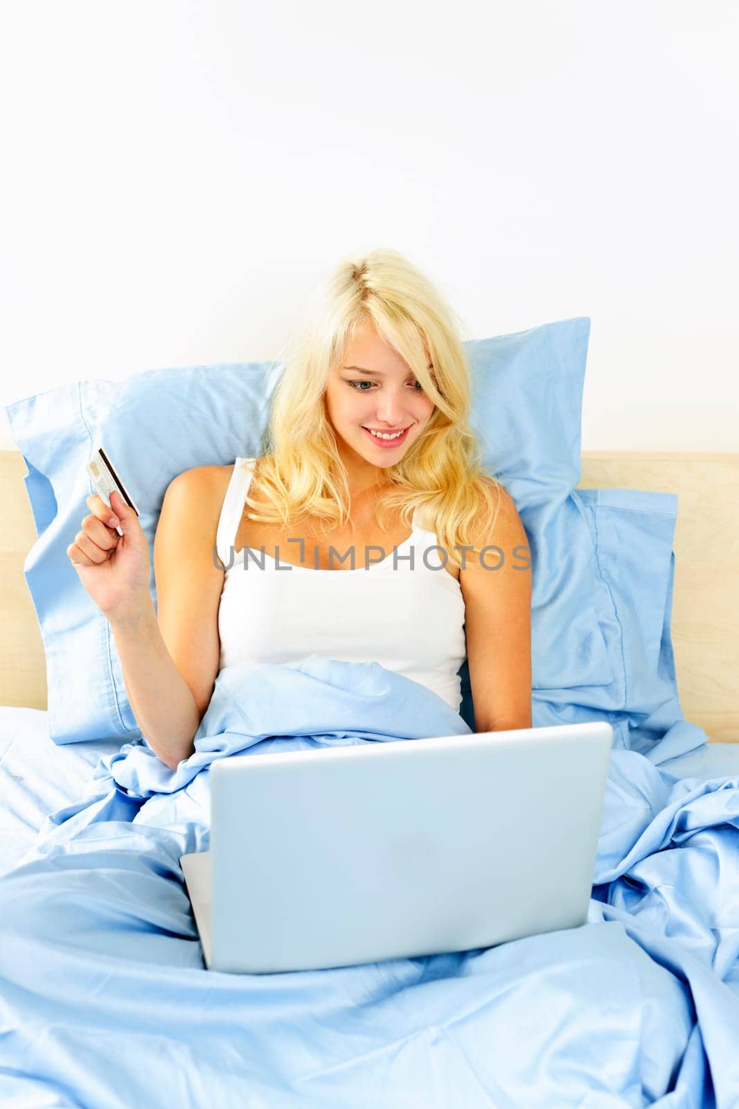 Happy blonde woman online shopping on internet in bed