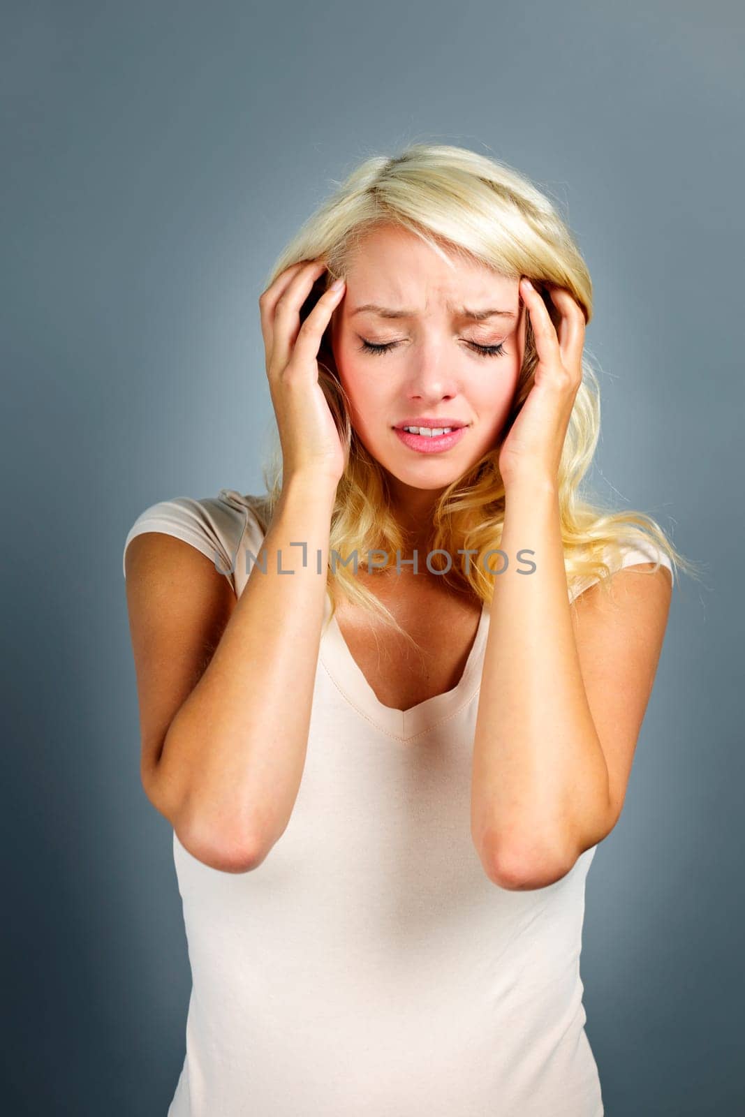 Upset young blonde woman with headache on grey background
