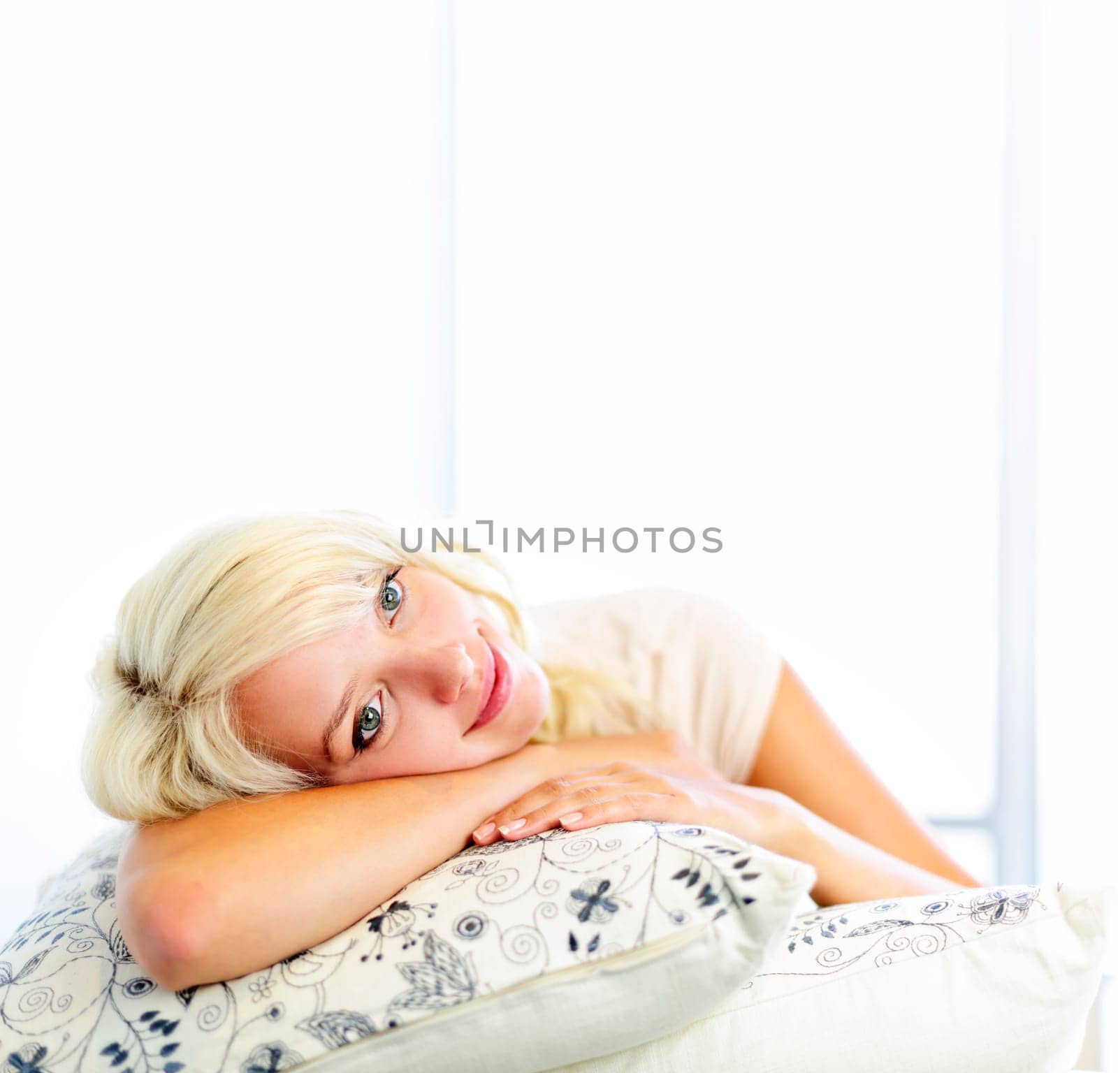 Portrait of happy blonde woman daydreaming and smiling on couch