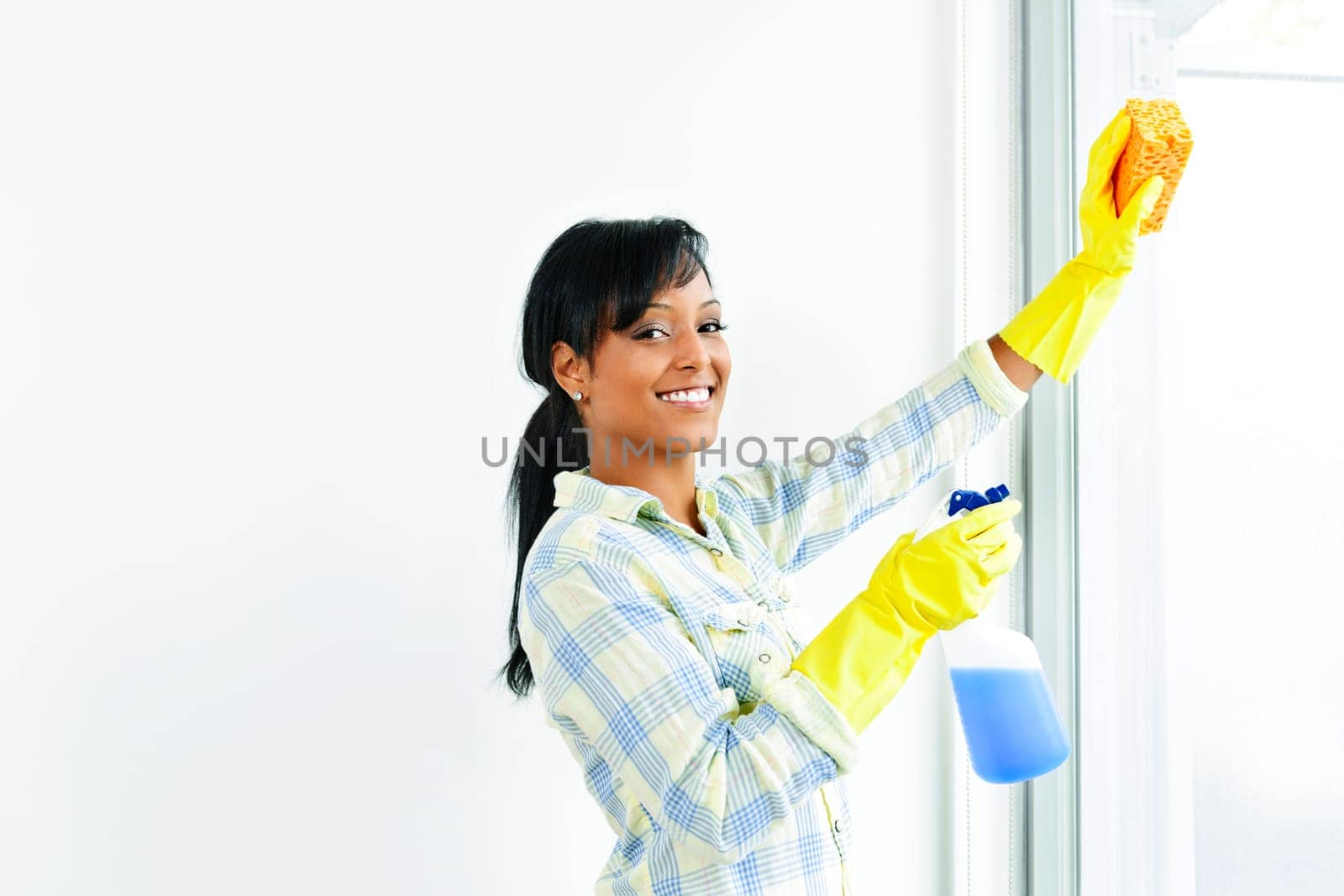 Smiling black woman cleaning windows with glass cleaner