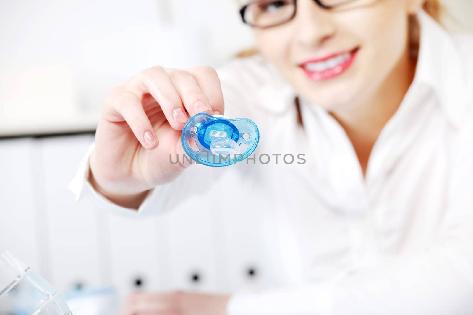 Caucasian businesswoman in glasses giving a dummy to her child in the office.