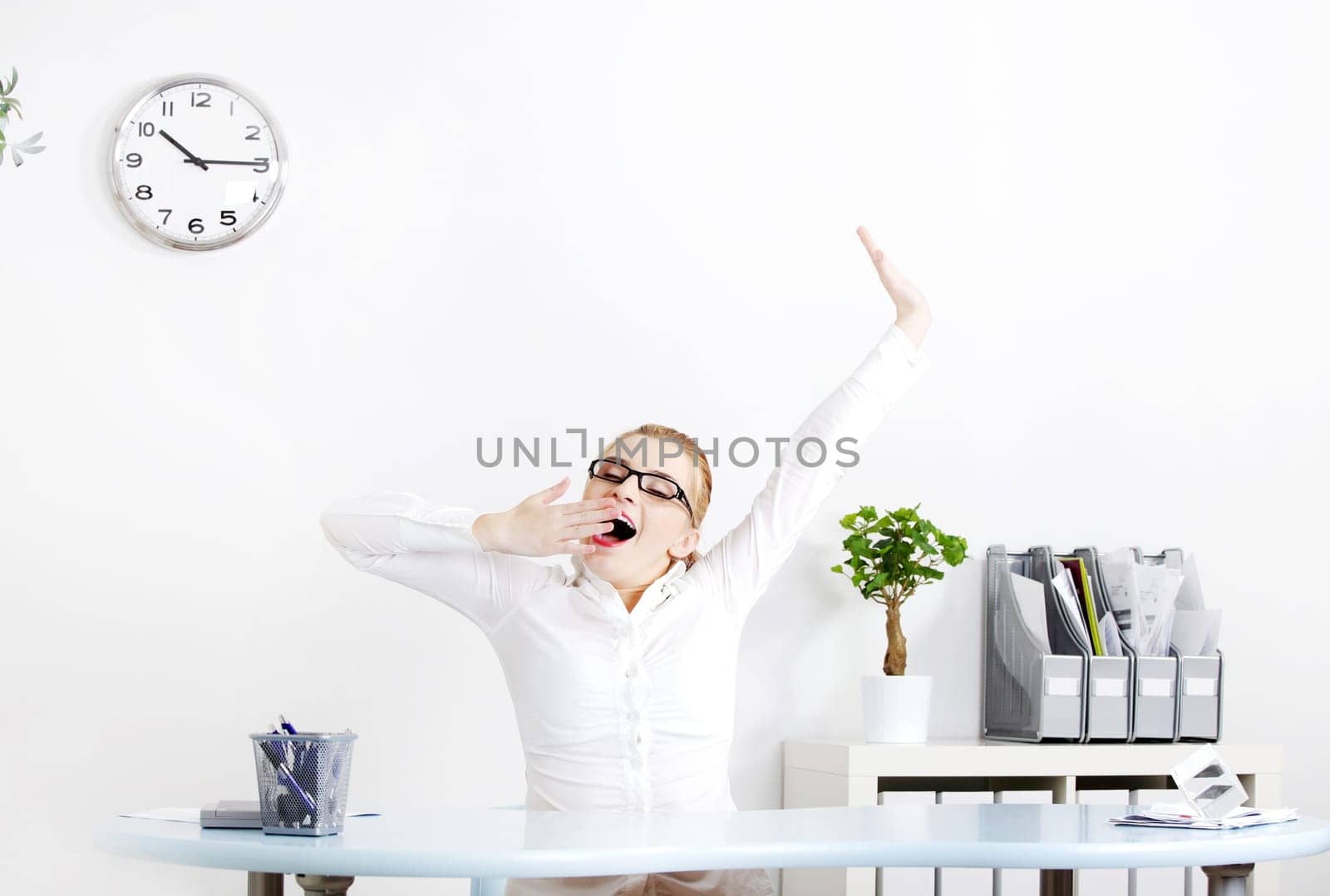 Blonde caucasian businesswoman in glasses yawning in the office.