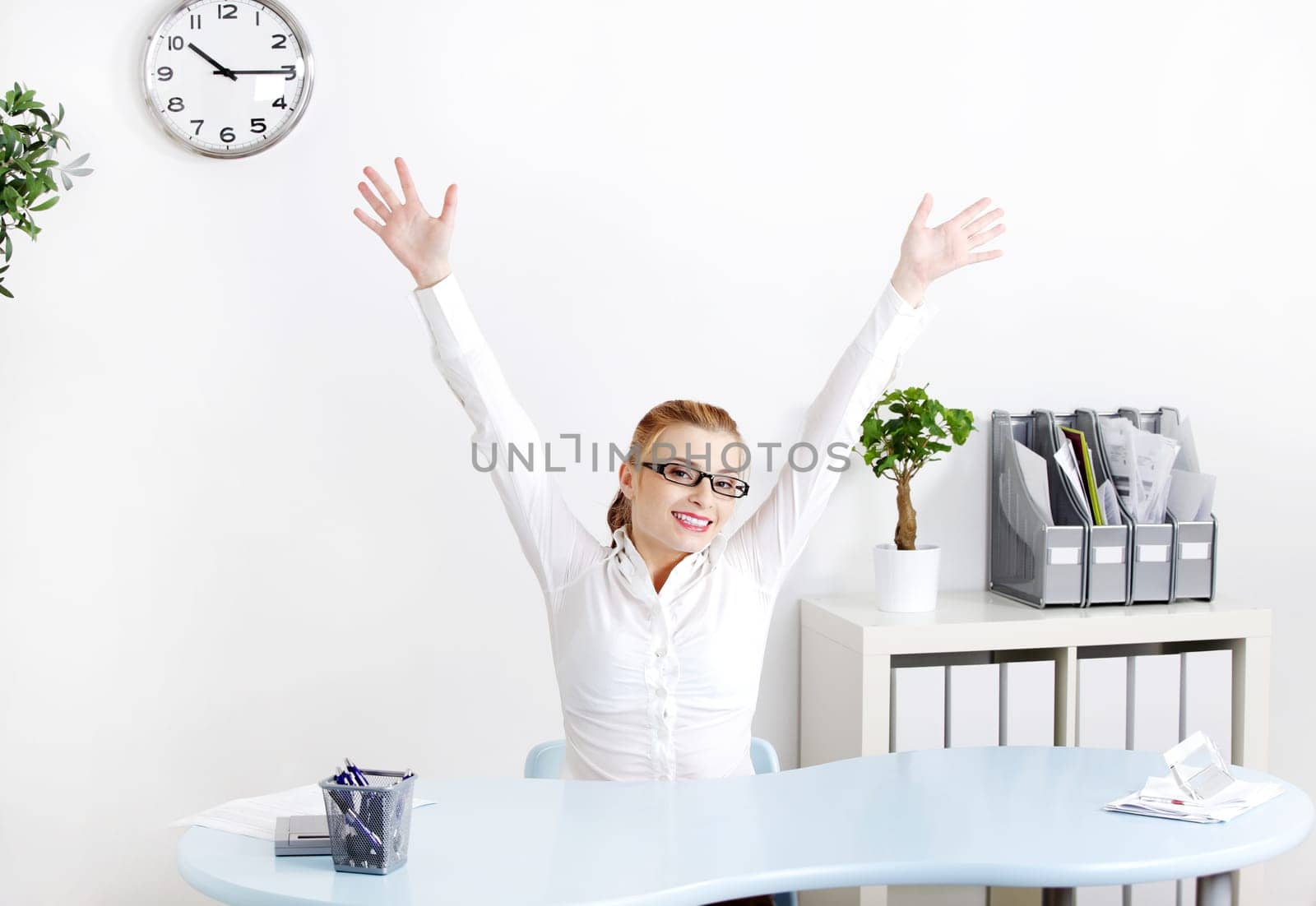 Young caucasian woman sitting in the office with her hands in the air.