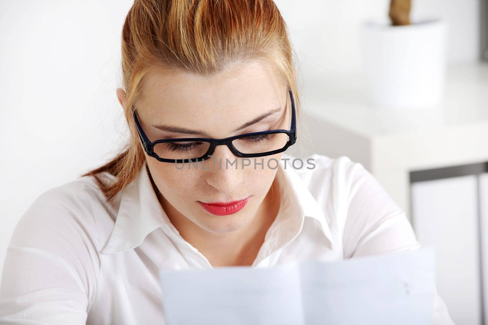 Closeup on young pretty woman in glasses reading files.