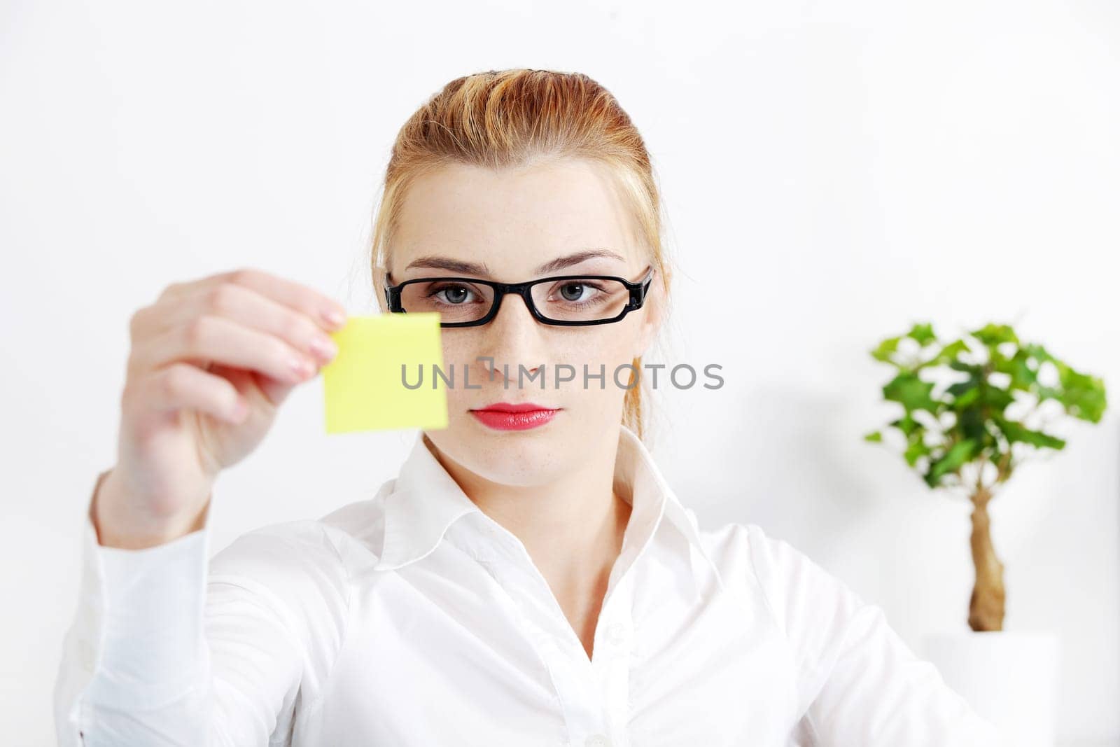 Young caucasian bussineswoman looking at yellow sheet of paper in the office.