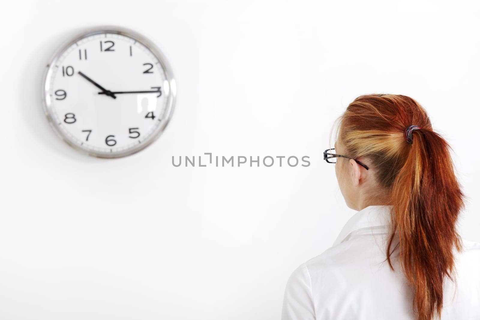 Caucasian businesswoman looking at white clock on the wall.