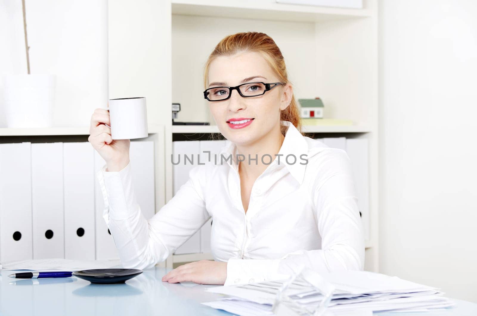Pretty caucasian woman in glasses holding mug in her hand sitting in the office.