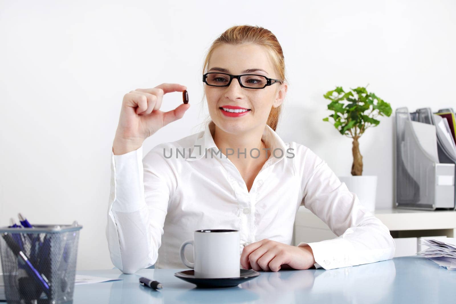 Smiling beautiful woman sitting in the office and holding a pill.