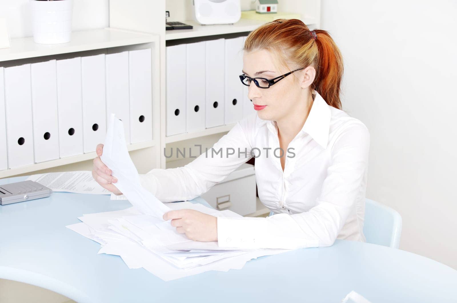 Sitting caucasian woman sitting behind the desk and reading files in the office.