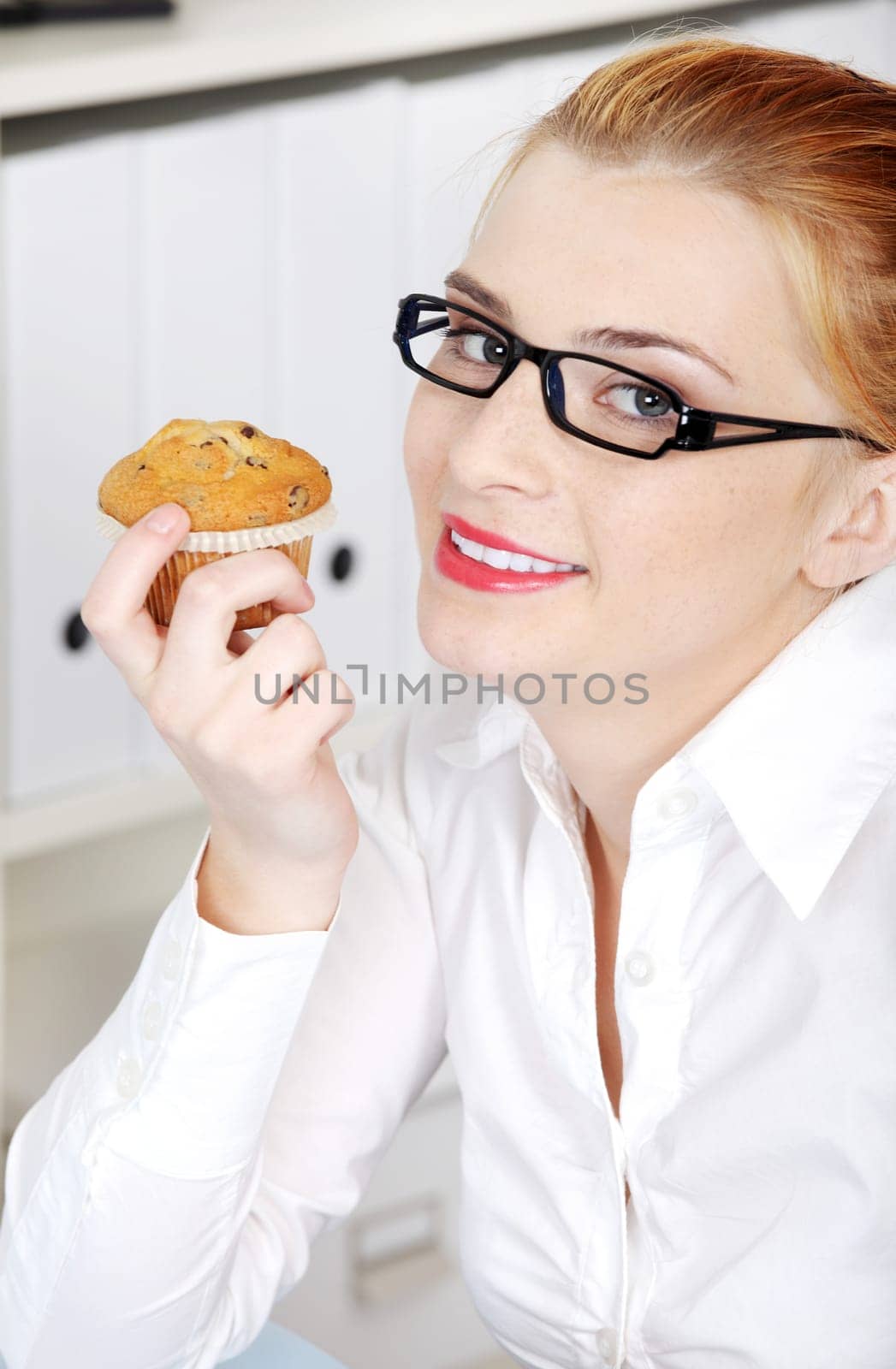 Closeup portrait of sitting woman in glasses holding a cupcake in the office.