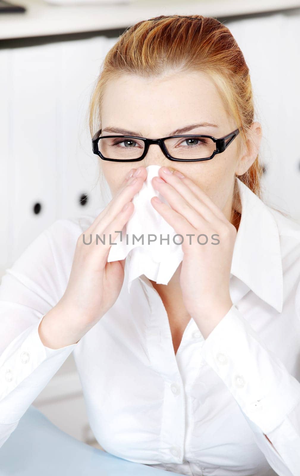 Young woman sneezing in the office.