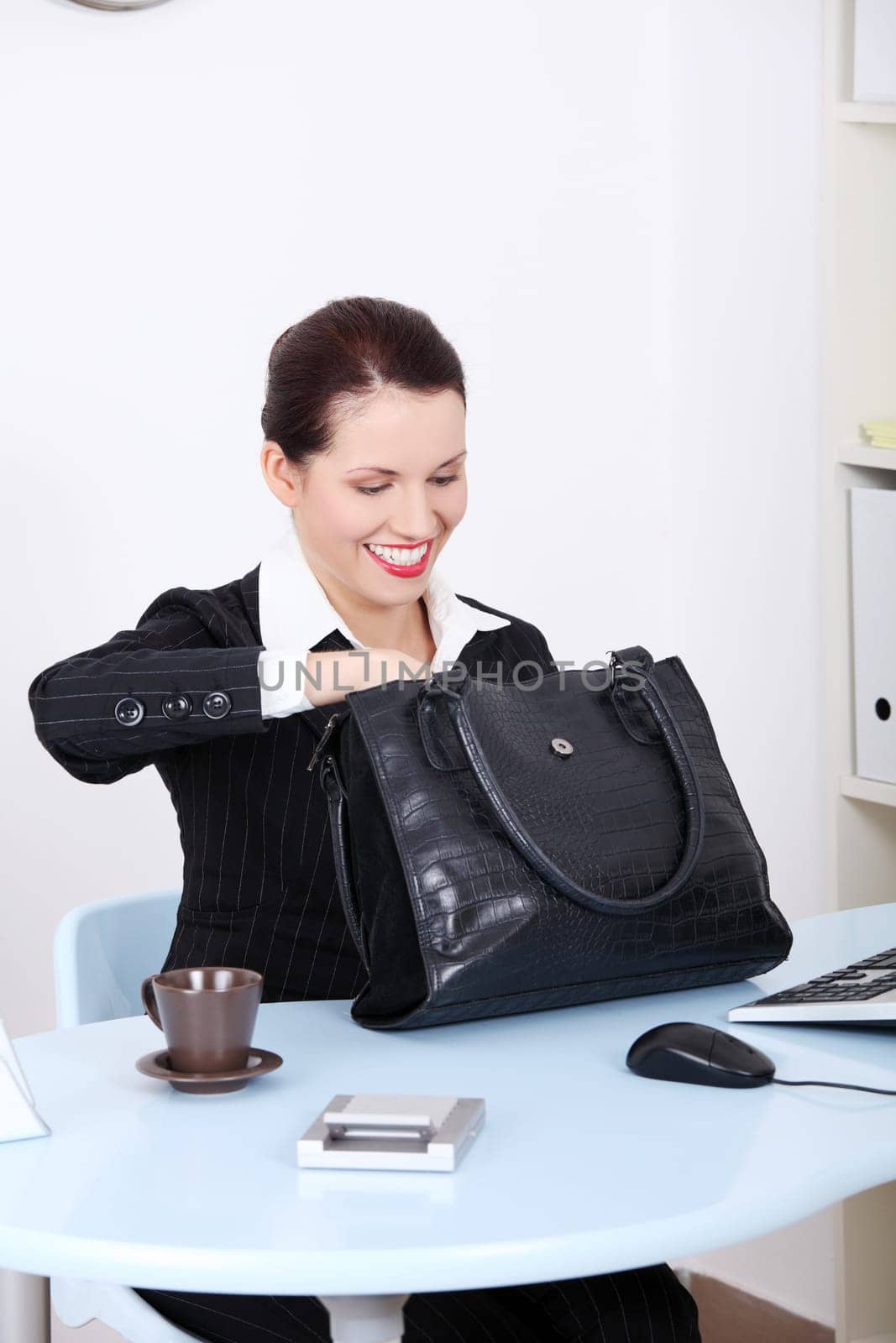 Pretty caucasian businesswoman searching in her black bag at the desk in the office.