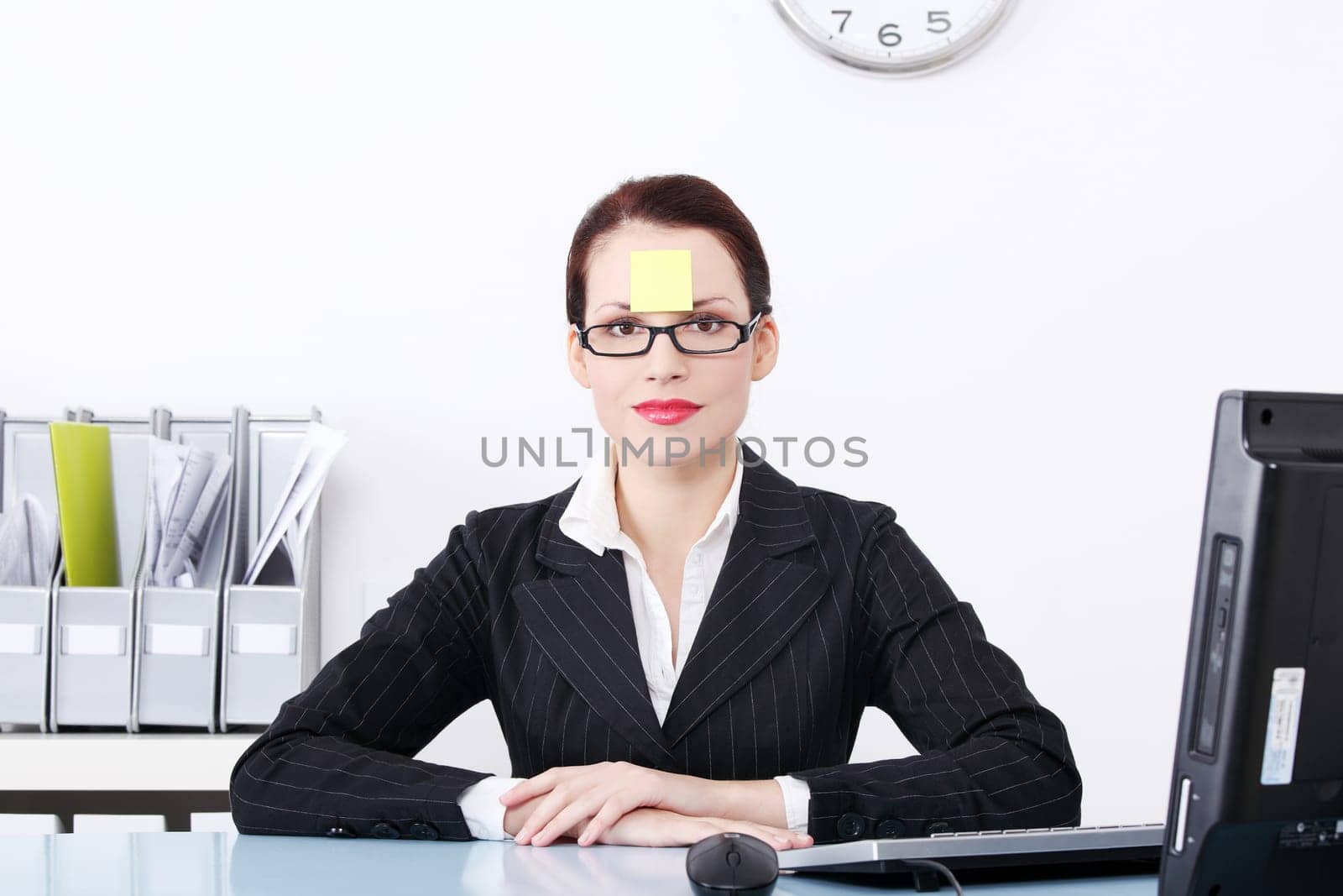Pretty caucasian businesswoman sitting in the office with post it note on her forehead.
