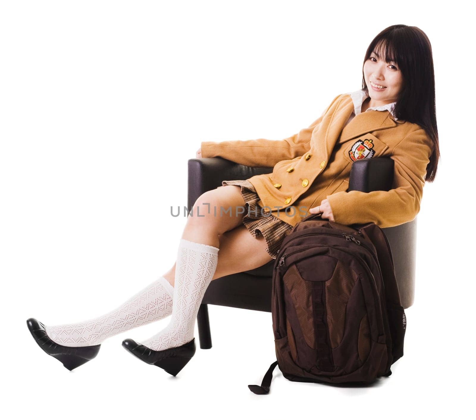 Female chinese student in a school uniform sitting in a leather chair with her bookbag.