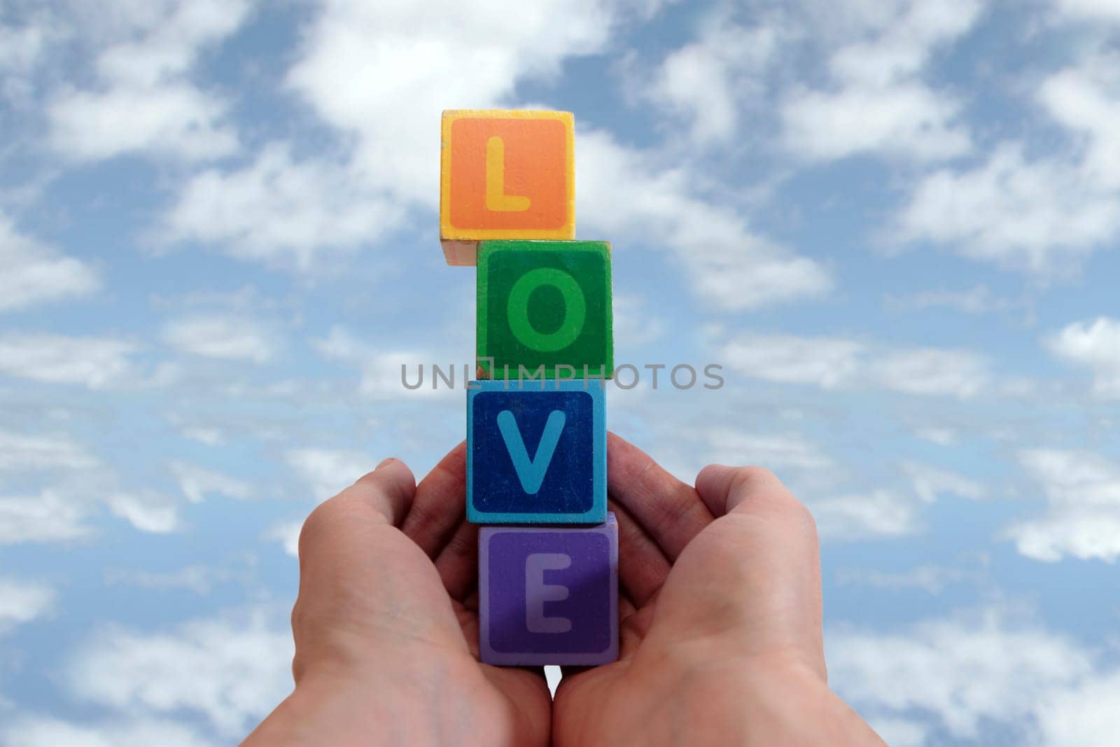 childrens toy letters in outstretched hands against cloudy background