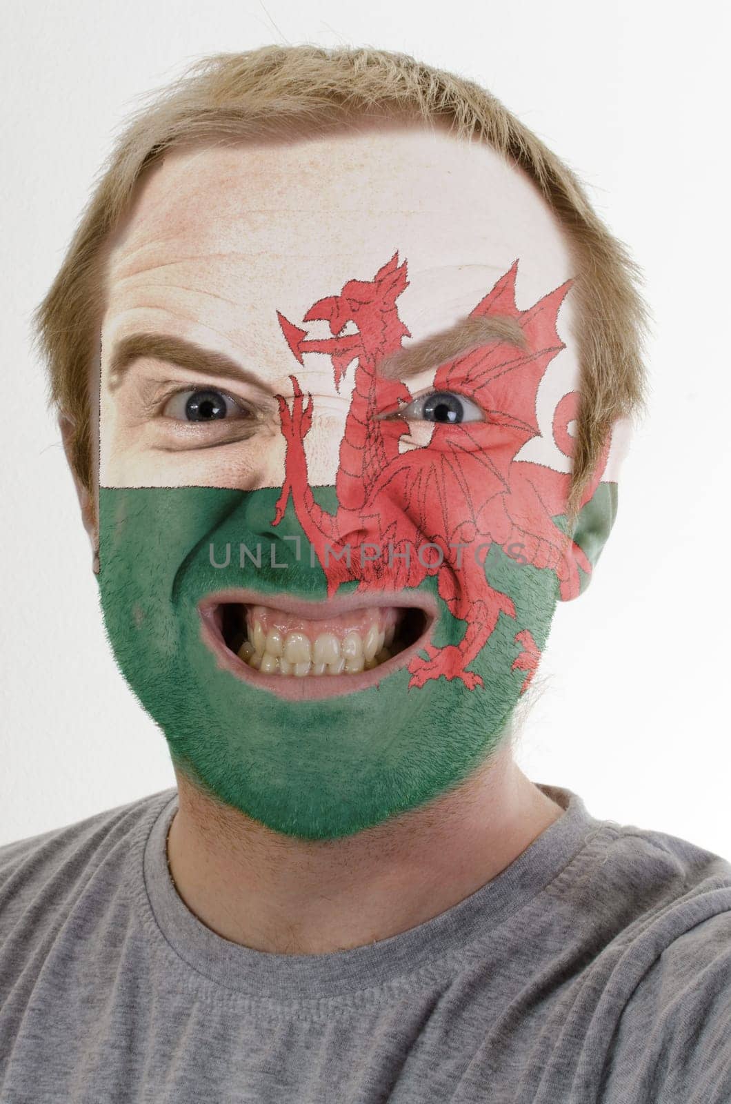 High key portrait of an angry man whose face is painted in colors of wales flag