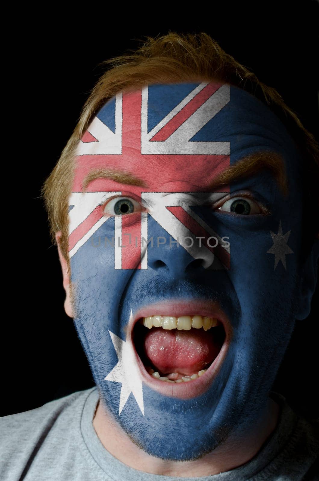 Low key portrait of an angry man whose face is painted in colors of australian flag