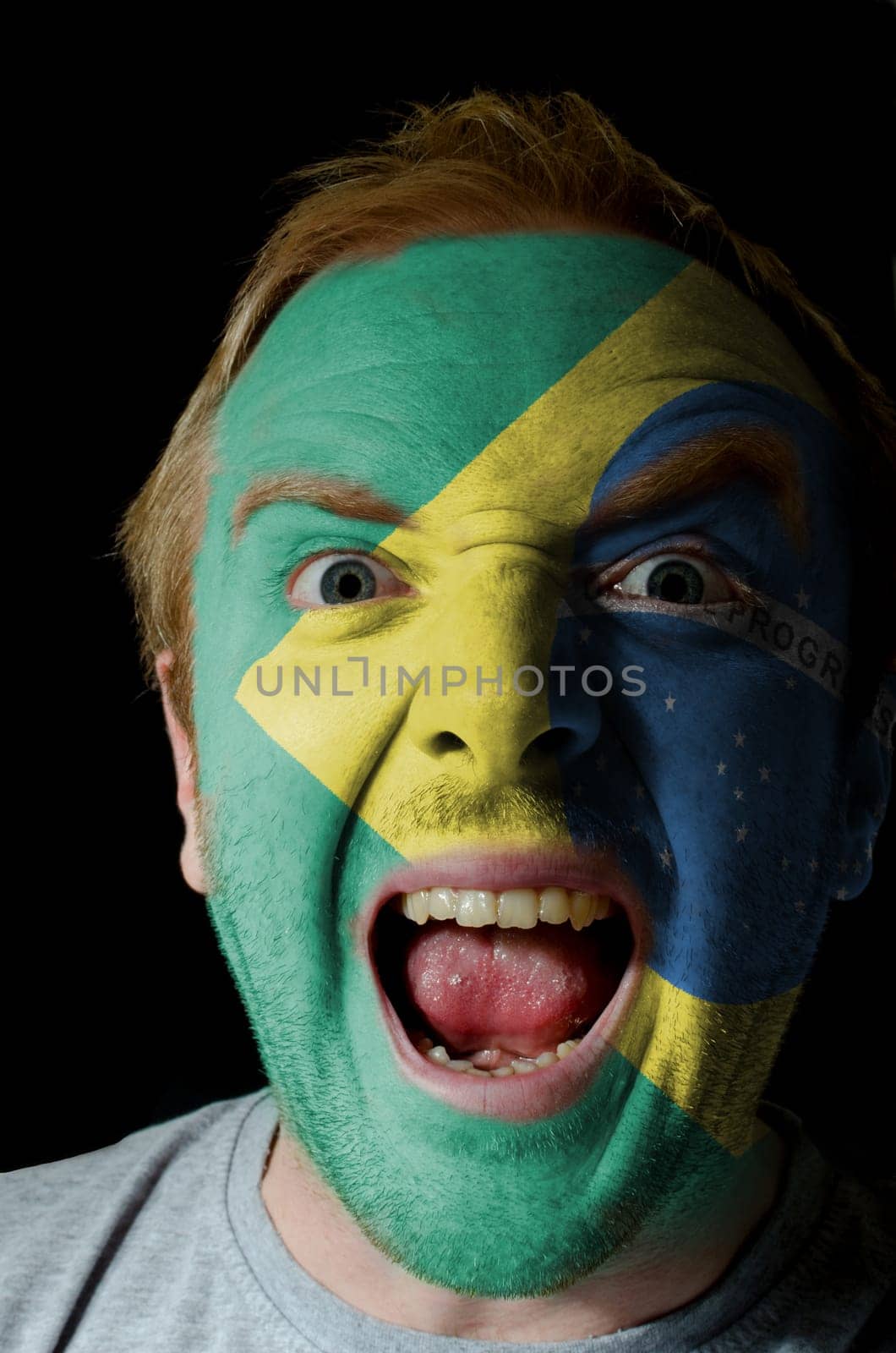 Low key portrait of an angry man whose face is painted in colors of brazilian flag