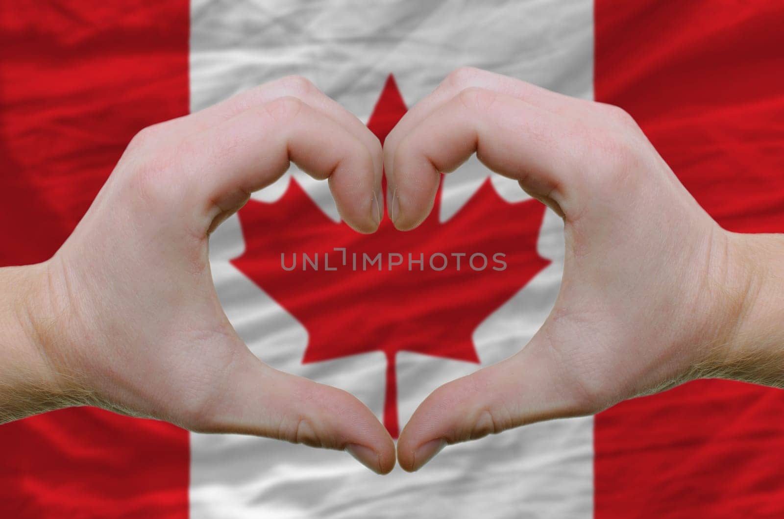 Gesture made by hands showing symbol of heart and love over canada flag