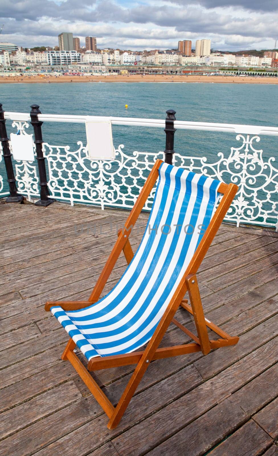 deck chair on Brighton pier boardwalk. empty sun lounger and views over sea towards cityscape of holiday resort in England