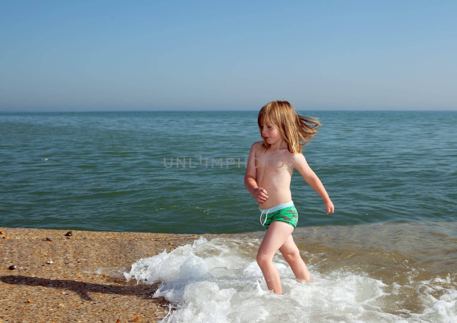 Child playing by water on beach in England. Boy in evening light on coast with waves