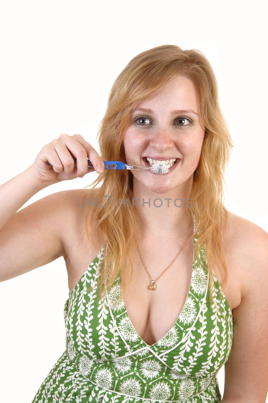 A young teenage girl in a green dress with a toothbrush in her mouth brushing her teeth, for white background.