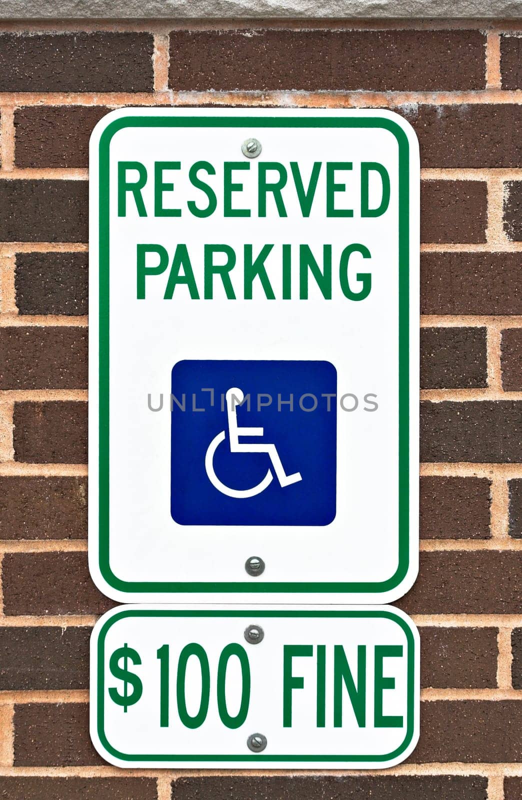 A reserved parking sign on a brick wall. There is a picture or symbol of a wheelchair on the sign along with a message for a one hundred dollar fine.