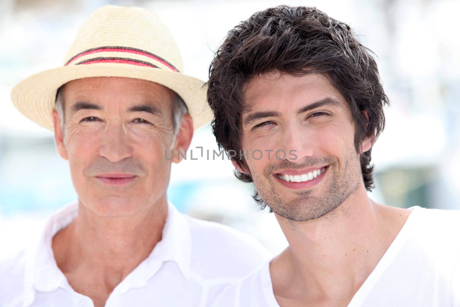 65 years old man wearing a straw hat and a 25 years old man posing in a summer vacation atmosphere