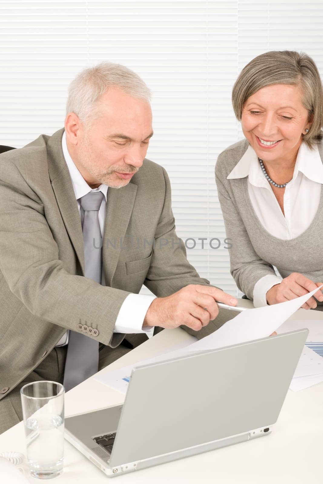 Professional elegant happy senior businesswoman looking graphs with man colleague