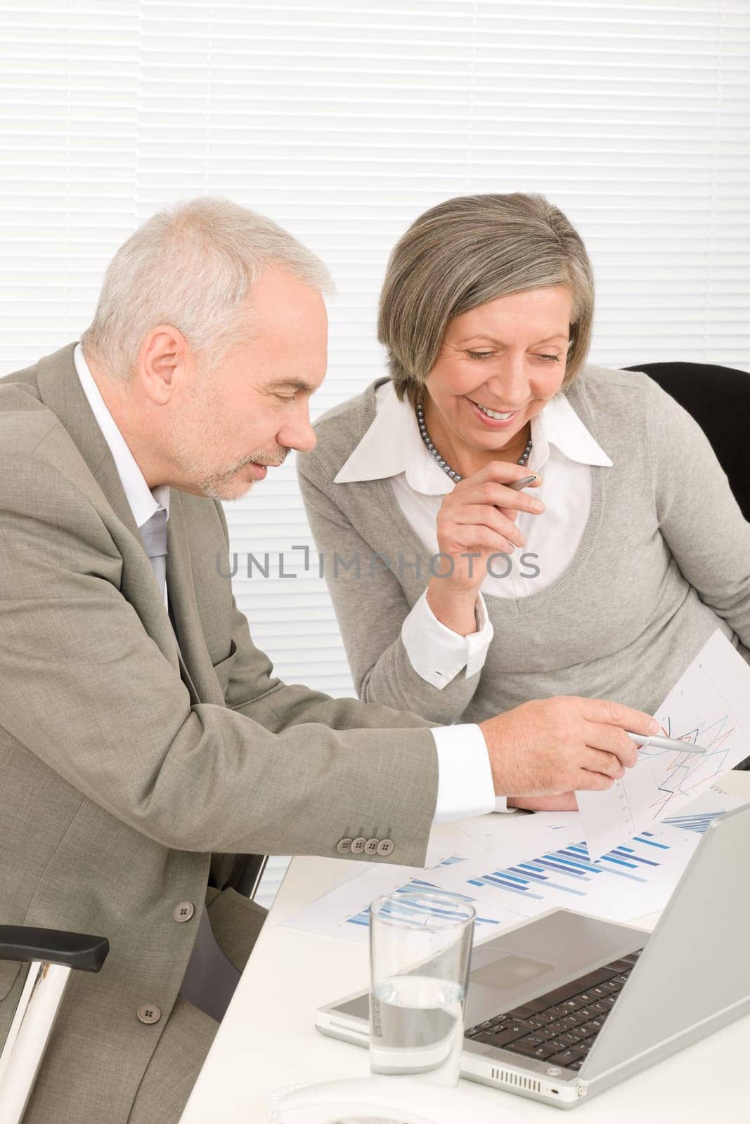 Professional elegant happy senior businesswoman looking graphs with man colleague