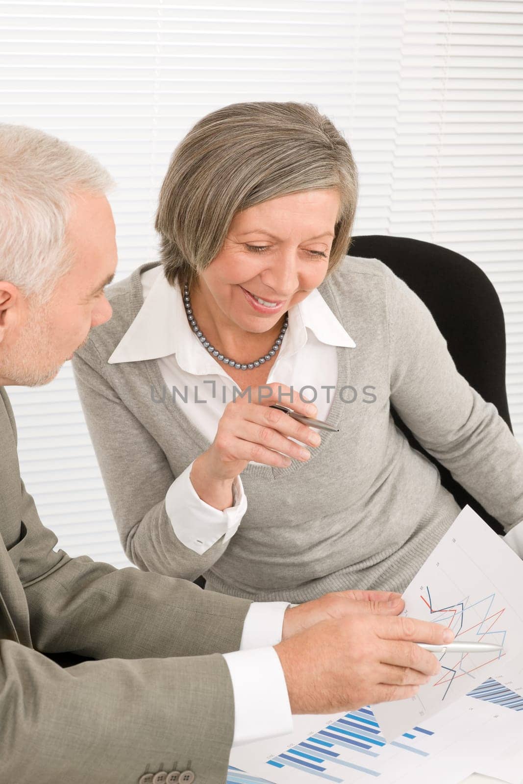 Professional elegant happy senior businesswoman looking graphs with man colleague