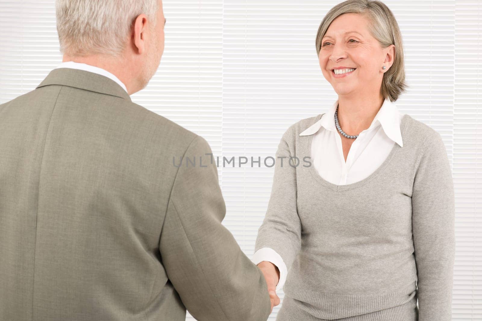 Professional elegant smiling senior businesswoman welcoming mature businessman