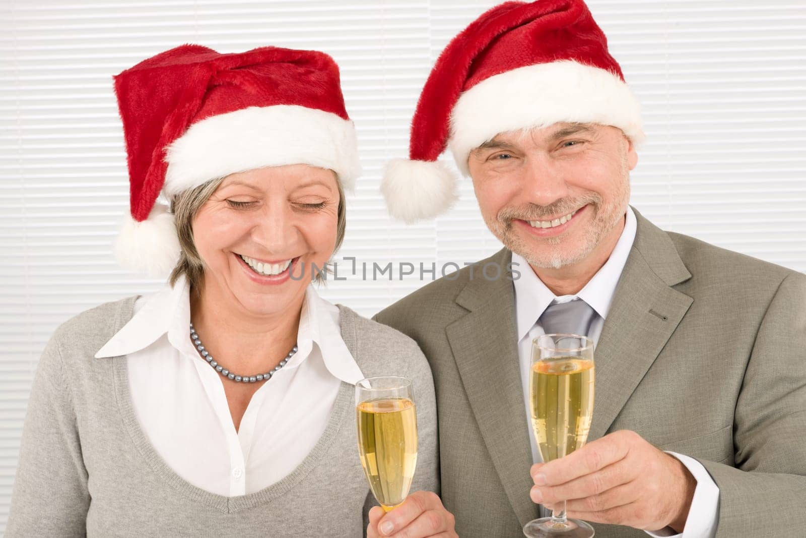 Laughing senior businesspeople in Christmas Santa hat drink champagne