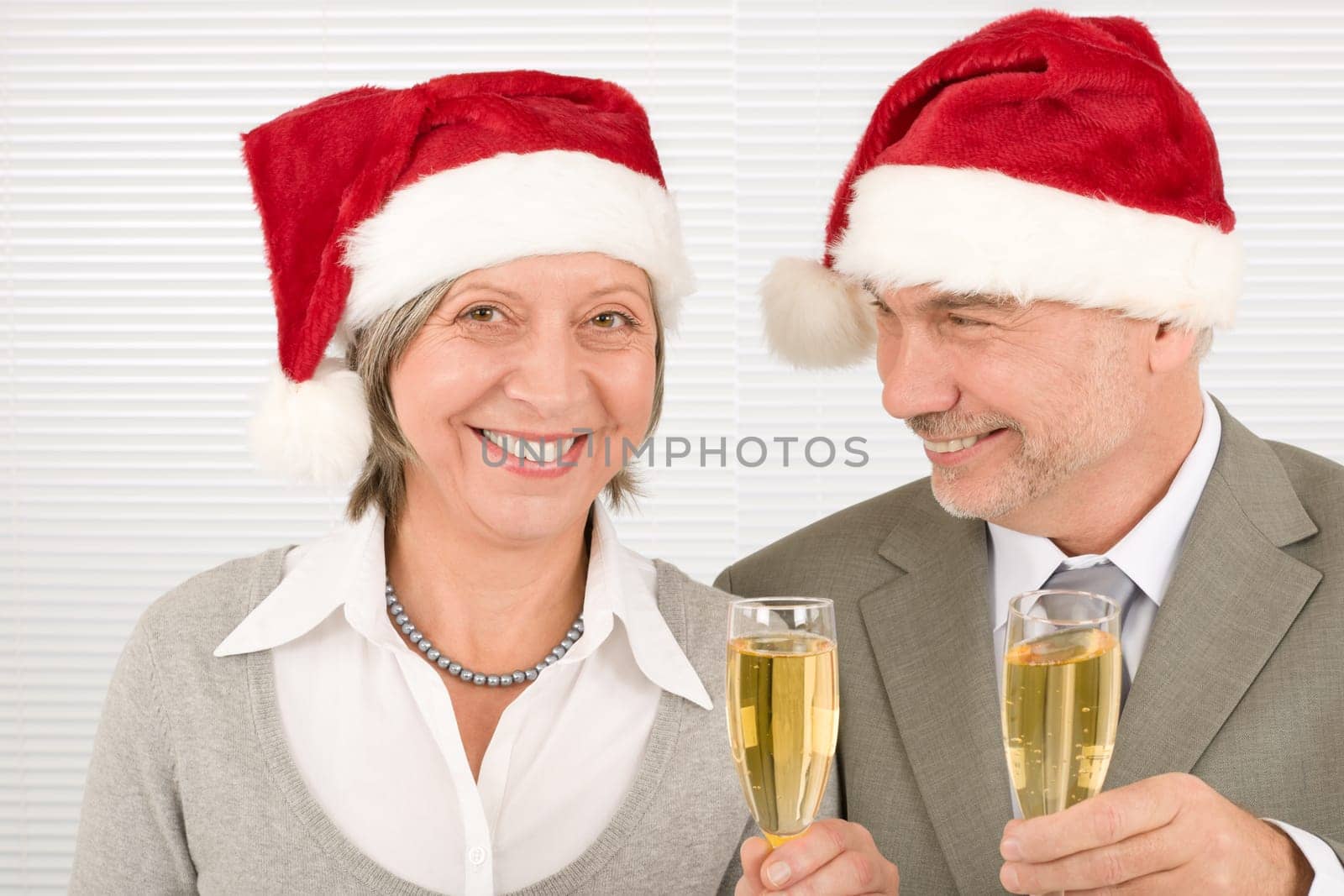 Laughing elegant senior businesspeople in Christmas hat drink champagne