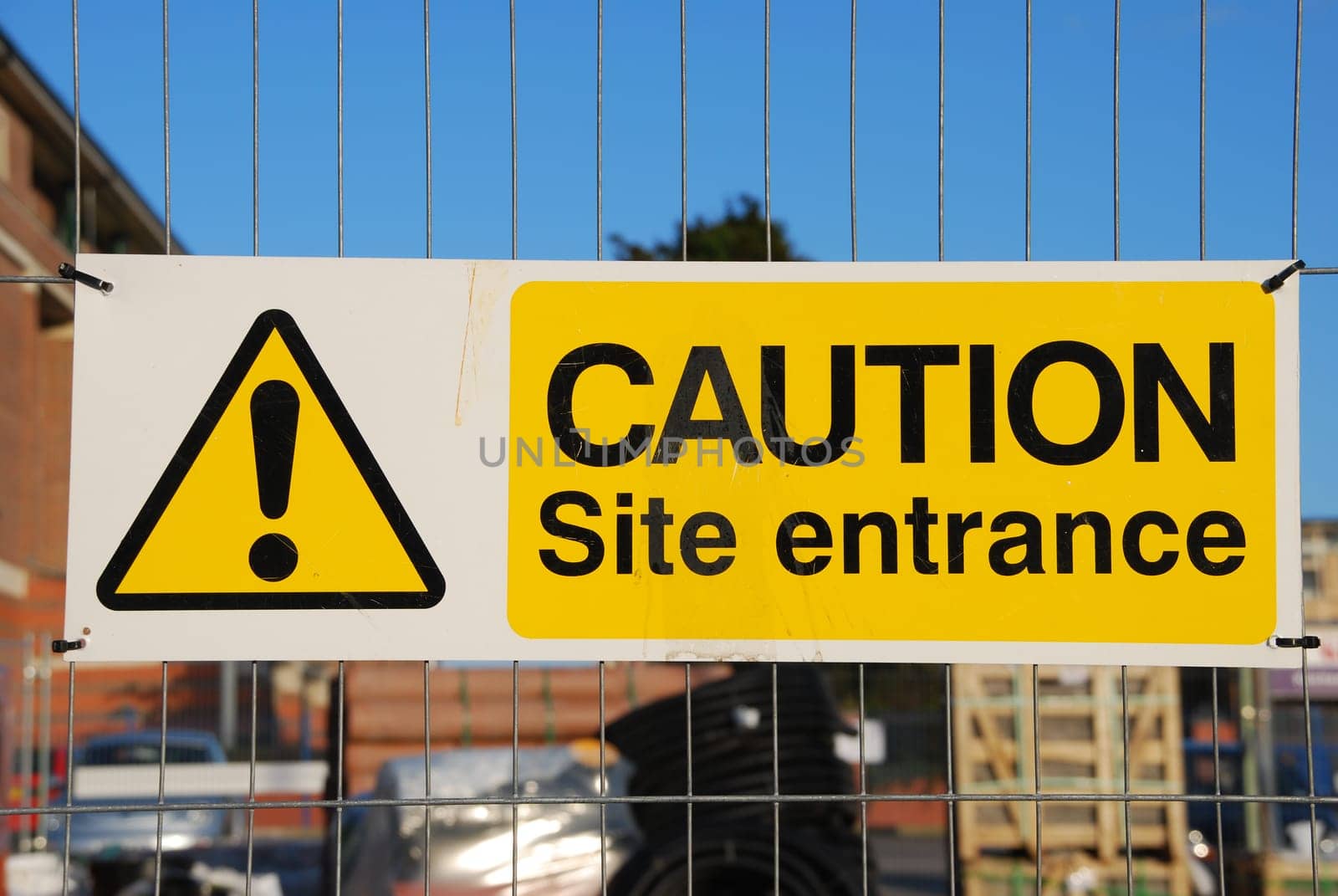 caution site entrance sign hanging on a metallic fence at a construction site