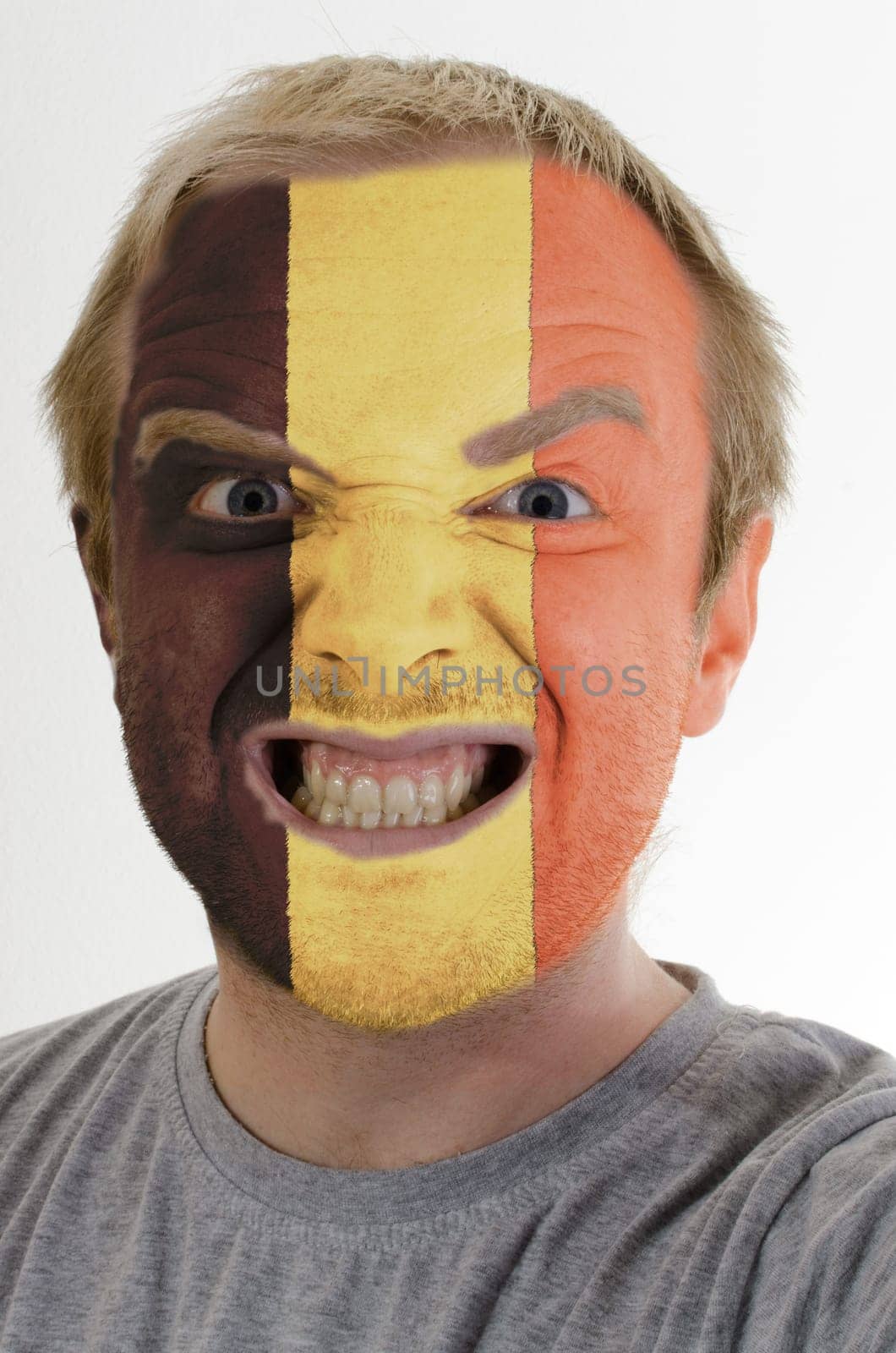 High key portrait of an angry man whose face is painted in colors of belgium flag