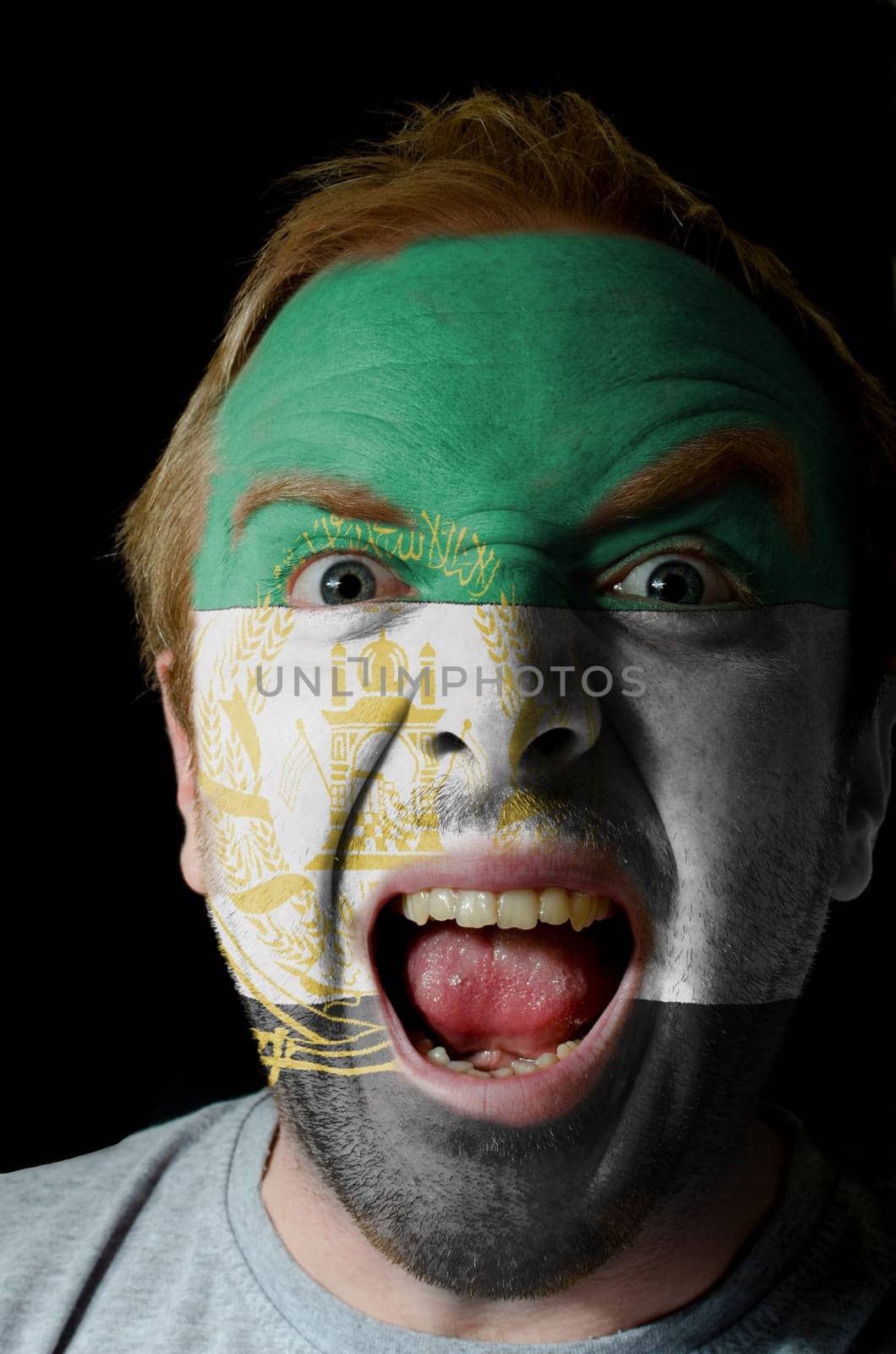 Low key portrait of an angry man whose face is painted in colors of afghanistan flag