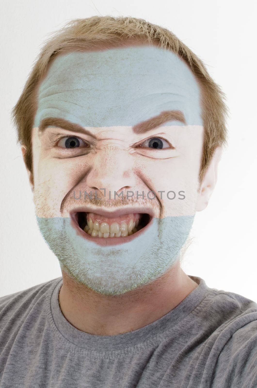 High key portrait of an angry man whose face is painted in colors of argentina flag