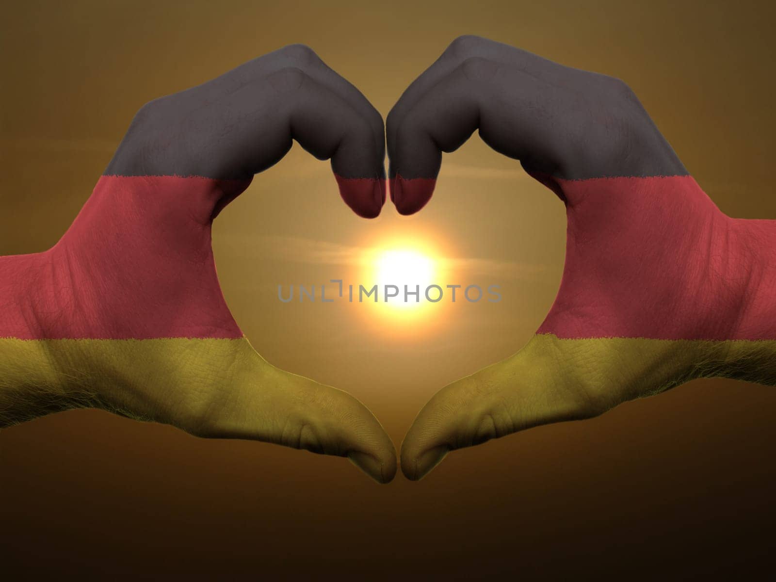 Gesture made by germany flag colored hands showing symbol of heart and love during sunrise
