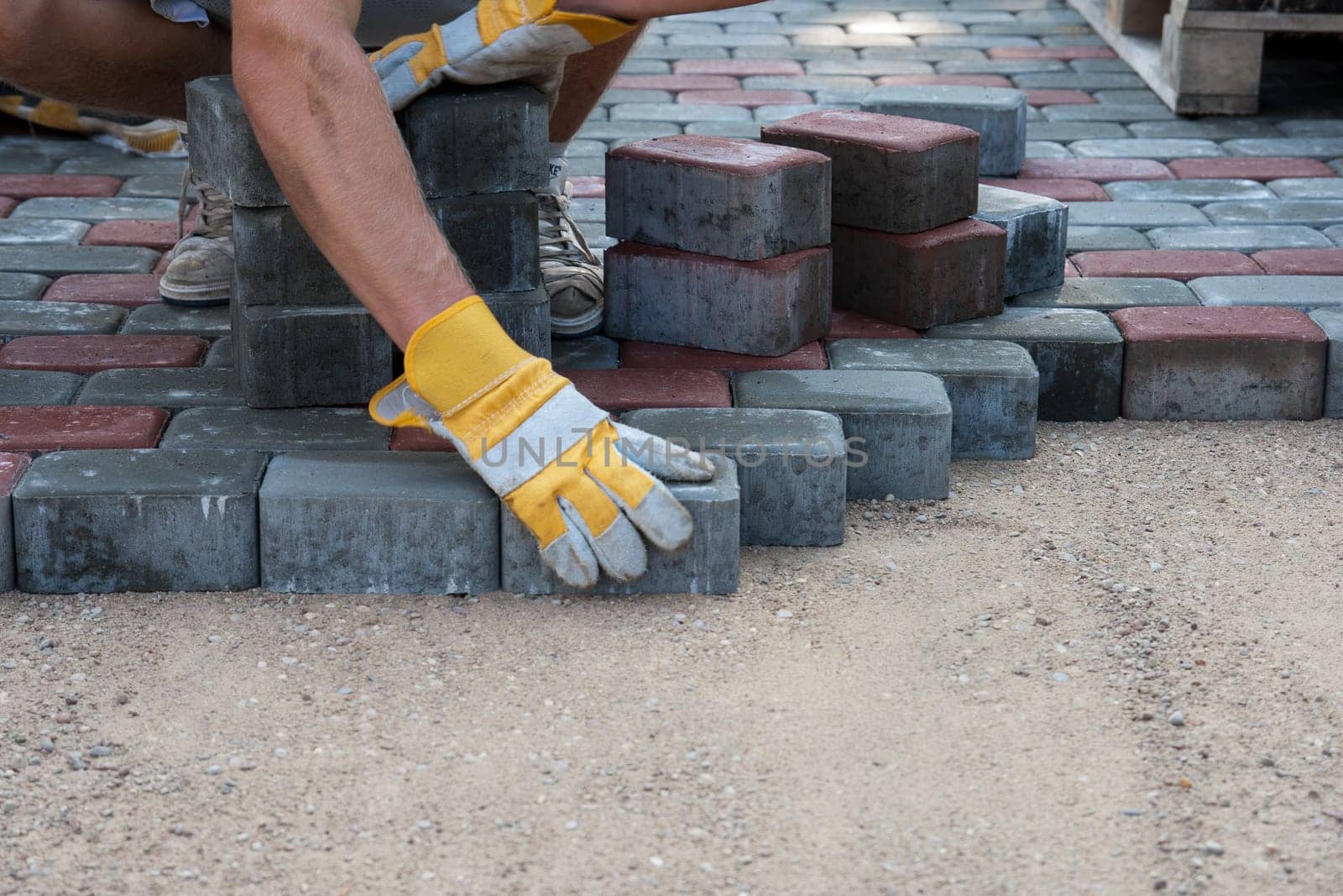 Pavers hands.Mason is building pavement. Hands in yellow gloves lays layers of bricks.