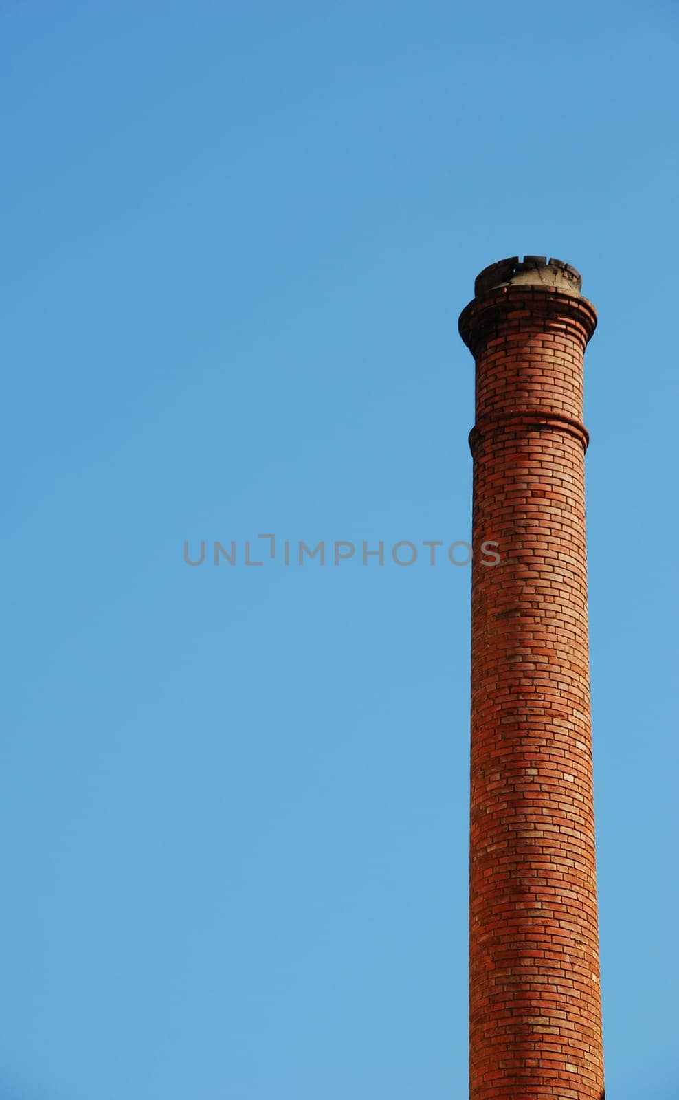 red brick industrial chimney against a blue sky background (plenty copy-space)