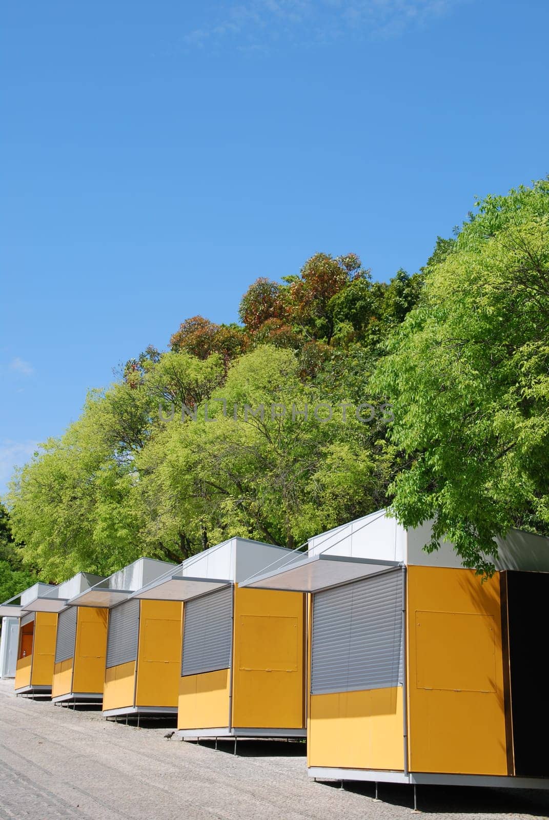 yellow kiosks shops against green trees and blue sky background