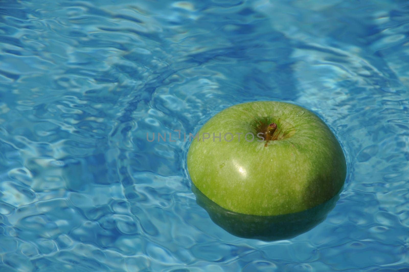 green apple floating at the swimming pool as a diet concept (healthy food and exercise)