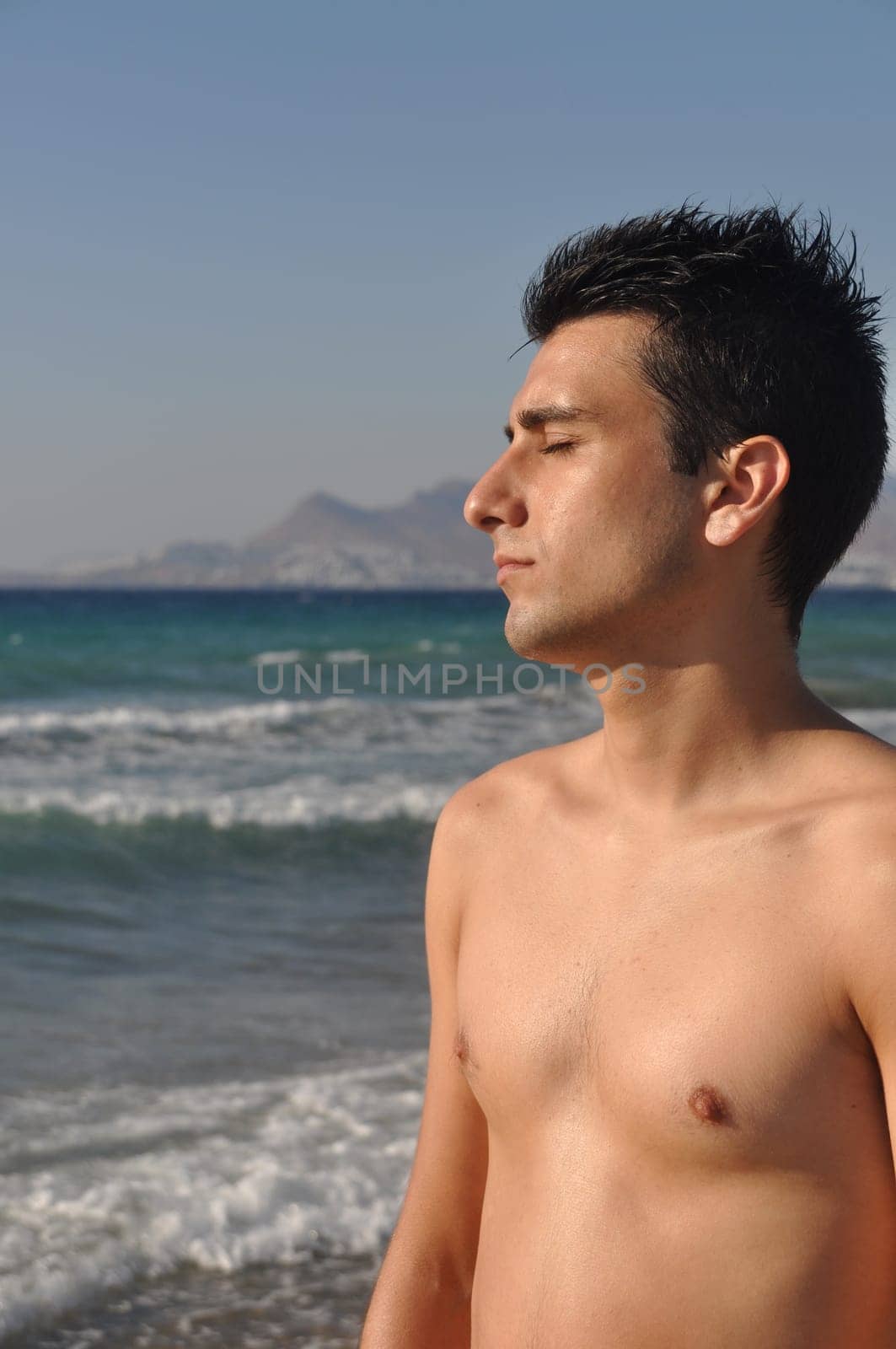 handsome young man getting suntan at Kos beach in Greece (blue sky)