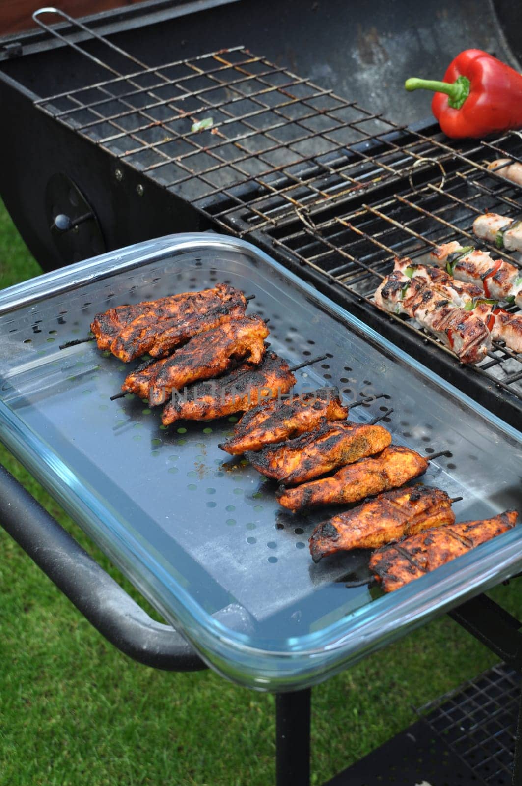 delicious chicken spits in a serving platter next to outdoor barbecue